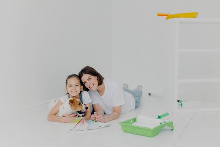Joyful friendly family members with dog lie on floor in empty room which needs improvement, choose color on palette sample, finish house redecoration, have good relationship. Teamwork, house choresの写真素材