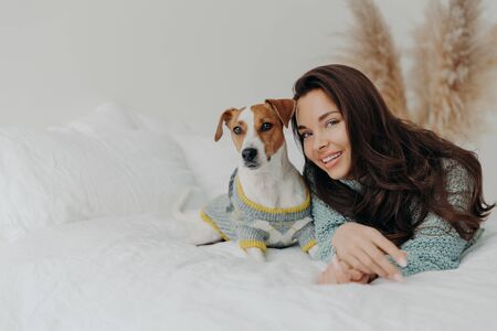 Best friends. Pleased attractive woman lies near jack russell terrier dog, expresses love and care...