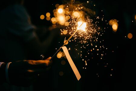 Bright festive sparkler in hand. Burning sparkle in darkness. Unrecognizable person holding glowing holiday sparkling hand fireworks, shining fire flame. Bengal fire against black backgroundの写真素材