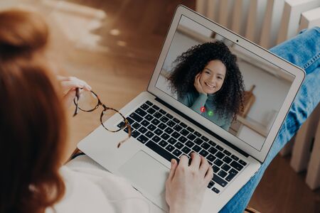 View from shoulder of woman greets best friend via laptop computer, exchange news and have online...