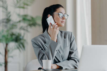 Photo of woman copywriter has telephone talk, looks aside, chats about ideas for new publication,...
