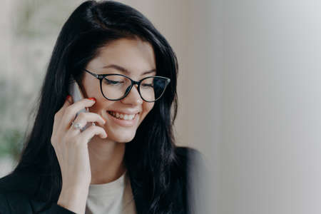 Happy woman lawyer keeps mobile phone near ear, has pleasant conversation with client, discuss...