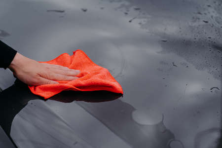 Mans hand cleans surface of black car with microfiber cloth. Maintenance and car wash concept....