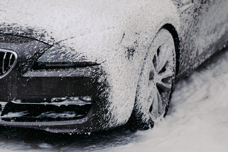 Modern black car covered by foam. Wash high pressure water and soap. Close up of auto on car wash station. Vehicle clean serviceの写真素材