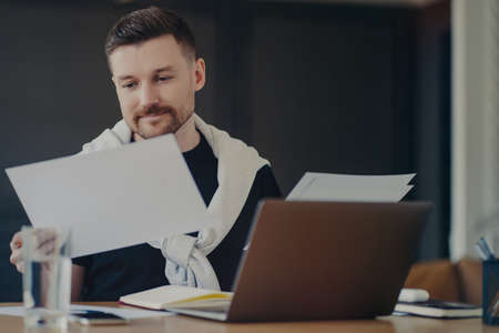 Pensive male freelancer or manager in casual clothes analyzing project documents and thinking about...