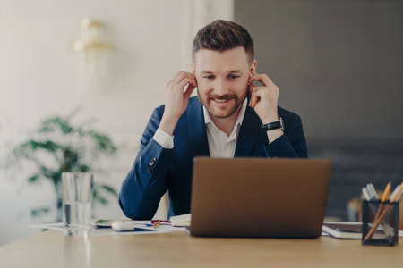 Happy businessman or male employer using wireless earphones and having online meeting, wearing...