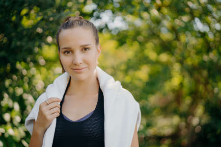 Lovely calm dark haired European woman wears black t shirt and white sweater over shoulders looks...