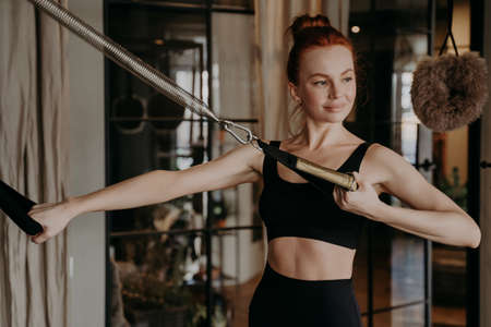 Training time of pilates female instructor on cadillac reformer, showing arm strengh exercises on machine with pretty smile during training in fitness studio. Healthy lifestyle and wellness conceptの写真素材