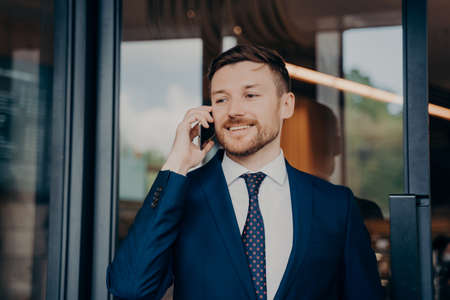 Young handsome businessman in suit talking on phone about important business, being satisfied by...