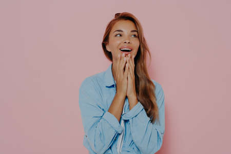 Excited woman with delightfully surprised look, touching both cheeks with hands, expresses positive...