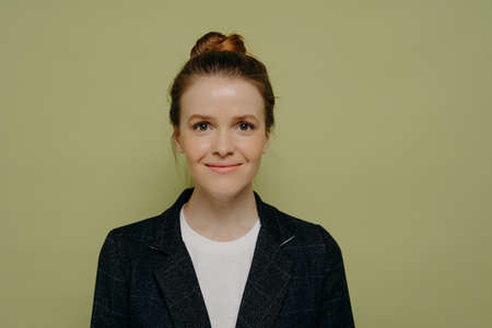 Studio portrait of beautiful happy young woman with hair in bun wearing casual clothes smiling and...