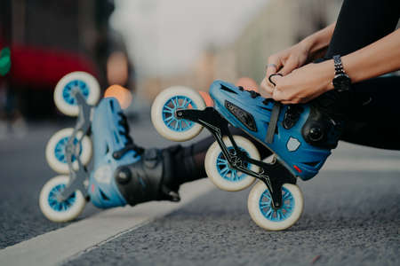Horizontal shot of faceless woman puts on rollerskates rides on road poses against urban background involdved in active sport. People hobby recreation extreme sport active lifestyle concept.の写真素材