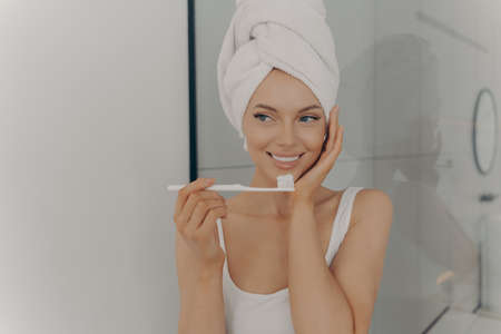 Attractive happy young girl with perfect white wide smile brushing her teeth in bathroom in front of camera after taking morning shower. Dental health and hygiene conceptの写真素材