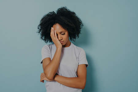 Portrait of upset African woman wearing casual clothes holding head with hand, having stressful look while suffering from migraine or headache. Unhappy female feeling frustrated, closing eyes tightの写真素材