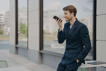 Confident businessman with smartphone using voice assistant app to organize his day or recording...