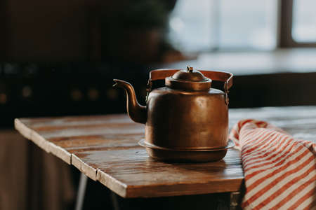 Horizontal shot of aluminium teapot on wooden table against blurred background striped napkin near. Old kettle made of bronzeの写真素材