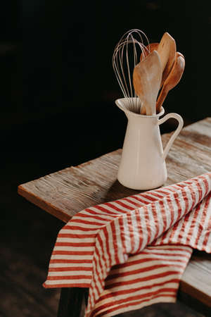 Vertical shot of vintage kitchen utensils in white ceramic jar on wooden table. Home kitchen decor. Kitchenware for cooking. Household itemsの写真素材