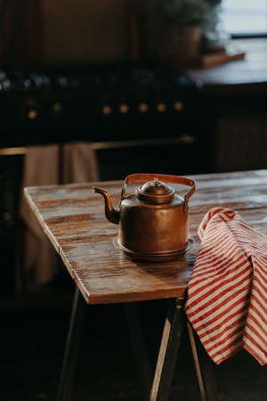 Vertical shot of steel kettle on wooden table in cozy room. Old ancient aluminium teapot to make tea. Vintage houseware.の写真素材