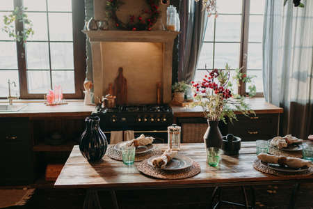 Interior of kitchen. Served dining table with plates glasses floral decor. Cutlery and glassware. Preparation for festive dinner. Table setting for family supperの写真素材