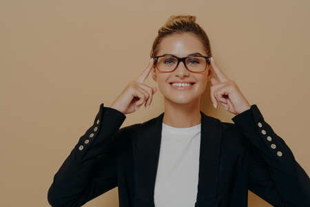Positive blonde female student putting on eyeglasses and holding them with hands, young beautiful caucasian woman posing and looking through spectacles at camera with beaming smile. Eyesight conceptの写真素材