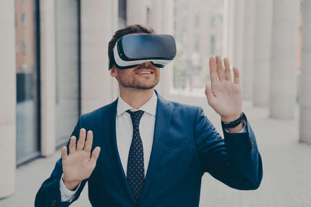 Young excited man in suit standing on city street and testing VR glasses or 3d goggles, impressed...