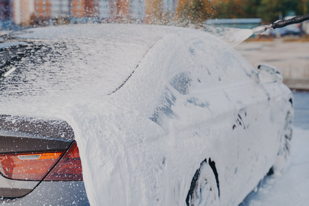Outdoor vehicle washing. Cleaning process of dirty car with high pressure washer at self-service station, luxury auto in white soap snow foamの写真素材