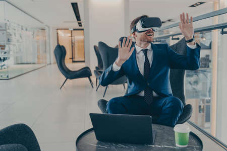 Exited CEO in VR headset enthusiastically testing app on laptop sitting in business centre lobby....