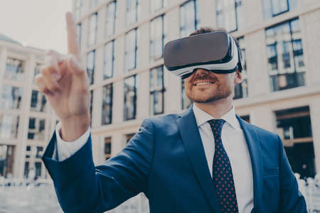 Businessman in formal blue suit using VR glasses outside, interacting with virtual world, trying to...