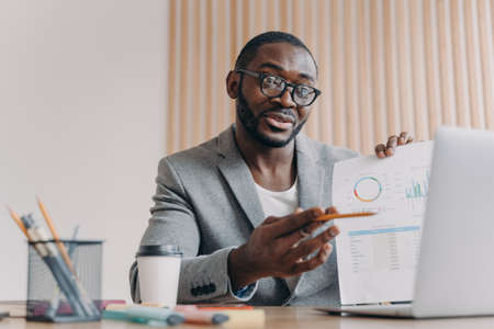 Young smiling african businessmen discussing income with partner via video call on laptop, pleasant afro american male ceo executive talking about project results during online meeting with teamの写真素材