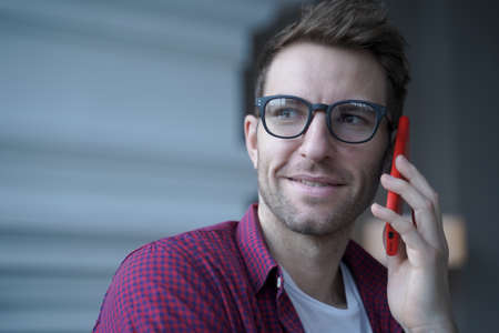 Millennial european man talking on smartphone while working distantly online from home,focused...