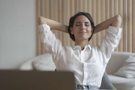 Attractive positive young female entrepreneur sitting at desk at home in relaxing position with...