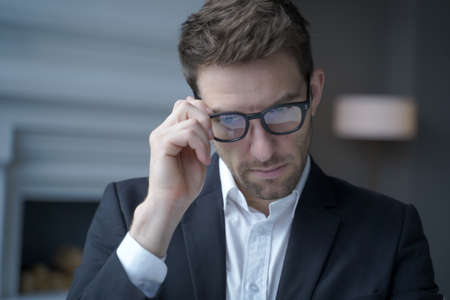 Close up of concentrated handsome austrian businessman dressed in suit adjusting glasses while working in office, executive man in spectacles at workplace. Business people conceptの写真素材