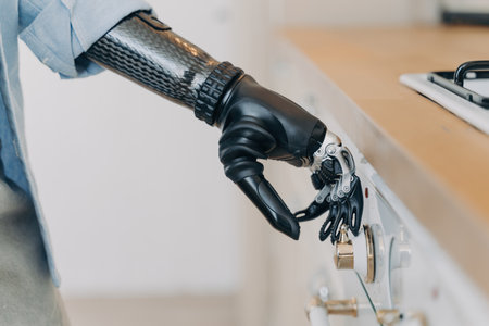 Disabled person's electronic cyber hand switches on stove in kitchen. Amputee with high-tech carbon arm, finger and wrist joint sensors. Daily routine of disabled individual.の写真素材