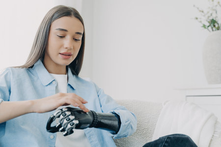 Handicapped girl explores bionic arm, presses buttons. Young European woman with cyber hand at home....