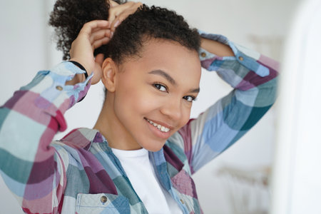 Smiling young mixed race girl embraces her natural beauty, holding and styling her healthy afro hair...