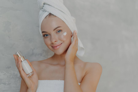 Beautiful woman with natural makeup applies face cream, clean skin. Beauty treatments concept on gray background.の写真素材