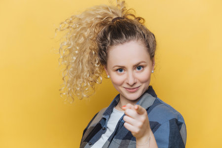Confident woman chooses you, dressed casually, pointing at camera indoors.の写真素材