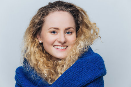 Pleased attractive woman with healthy skin smiles after date, isolated on blue background.の写真素材