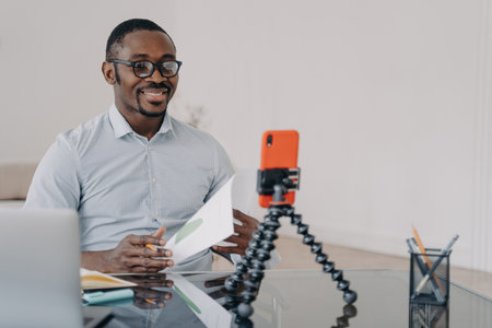 Black businessman: video call, smartphone. Smiling coach consults clients.