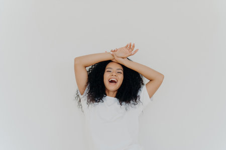 Overjoyed curly-haired lady, hands on forehead, laughing with mouth wide open, energetic vibes. Casual attire, white studio backdrop. Hilarious joke!の素材