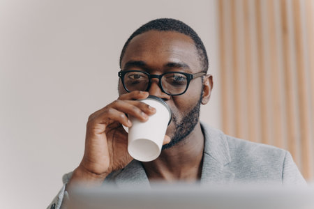 Confident Afro American CEO, takeaway coffee, laptop screen, remote financial meeting, video conference.の写真素材