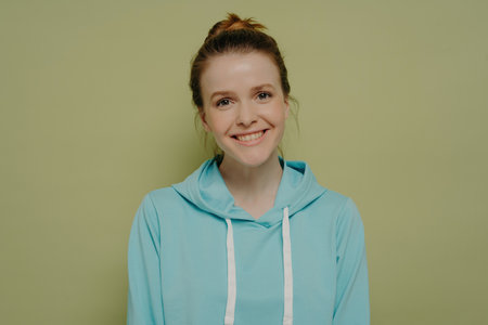 Attractive teen girl in urban hoodie, hair in bun, smiling with kindness, expressing positive emotions in studio.の写真素材