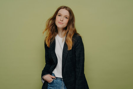 Stylish young female student in fashionable clothes, posing with hand in pocket on colored background. Charming teenage girl expressing positive emotions in casual attire.の写真素材