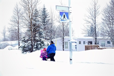 Mother and daughter carry the baby in a stroller through the snowの写真素材