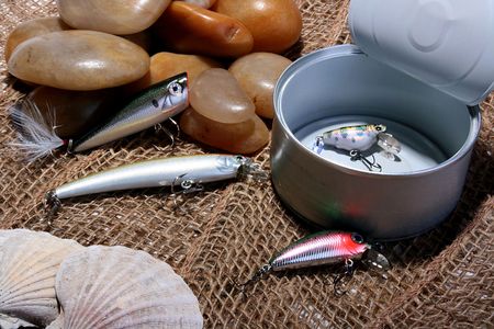Open can with the spoons hook for fishing. Sea stones and cockleshells against a rough sacking.の写真素材