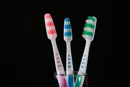 Three tooth-brushes with green and red bristle on black background.の写真素材