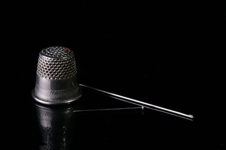 Thimble for protection of a finger during sewing, needles and a pin on a black brilliant surface.の写真素材