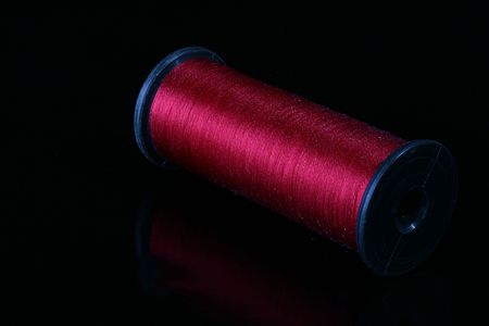 Darkly red threads on the coil for industrial use. Threads are placed on a black reflecting...