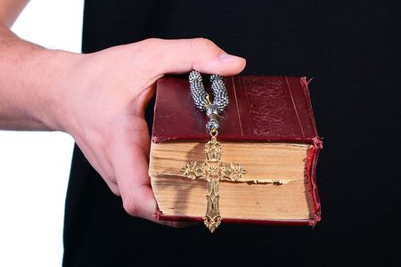 The man's hand holds the old bible with a cross on a chain.の写真素材