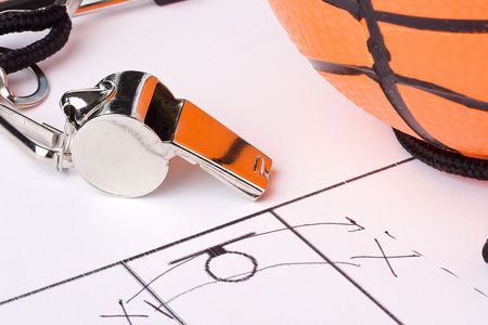 A silver whistle laying next to an orange basketball and the drawing of a game plan.
